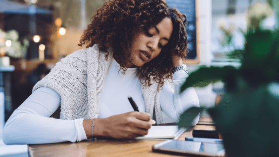 Black woman writing in a notebook looking pensive