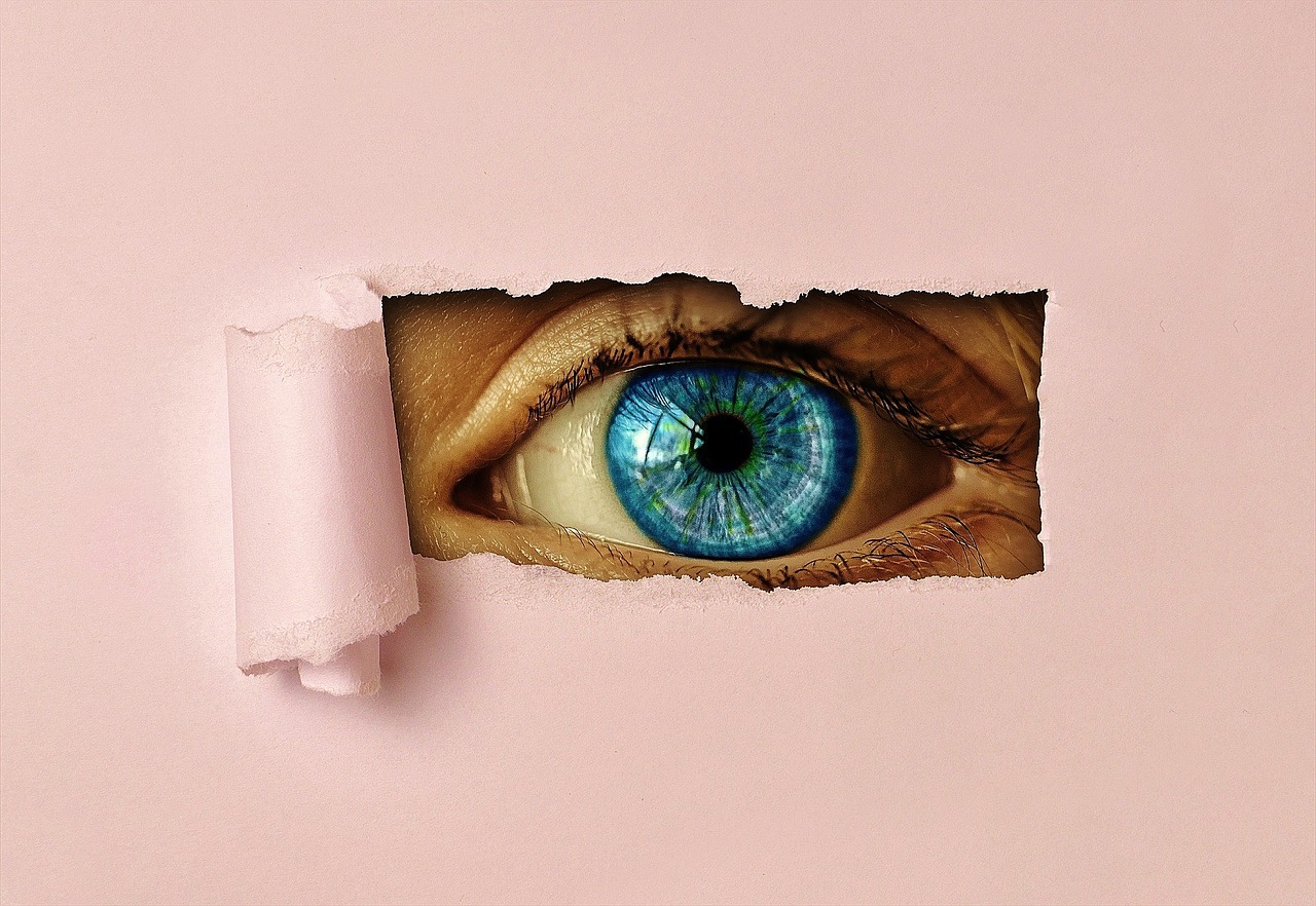 eye staring through hole in pink paper