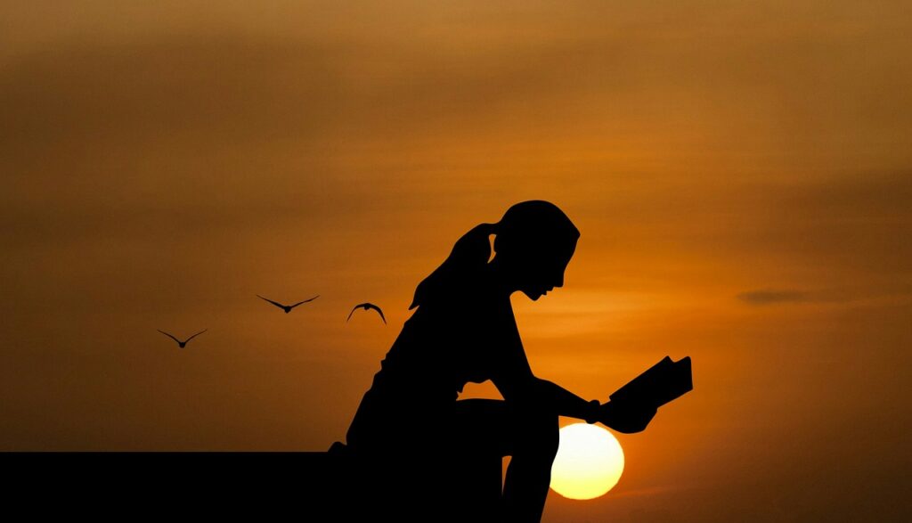 silhouette of a woman in front of the sunset, reading